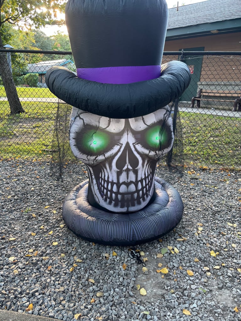 Inflatable skull decoration with glowing green eyes, black top hat, and purple band, displayed in a residential yard