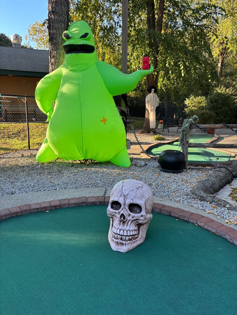 Bright green inflatable alien figure with waving arm next to miniature golf course with skull obstacle